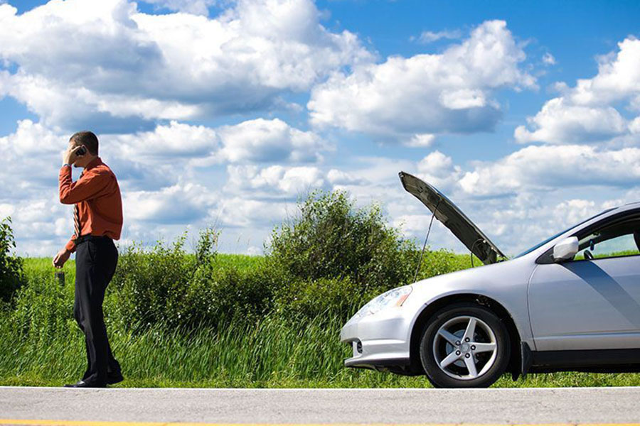 Man on cellphone standing next to car parked on shoulder with hood raised